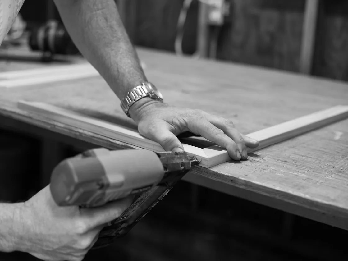 Manos trabajando una moldura de madera sobre el banco de un taller de enmarcado